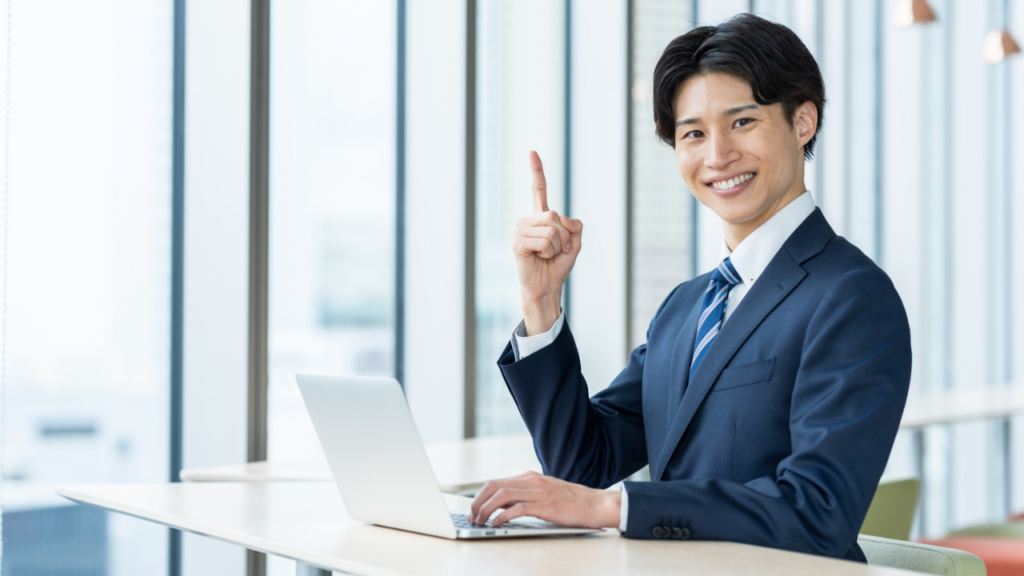 パソコンを開いて人差し指を立てるスーツ姿の男性