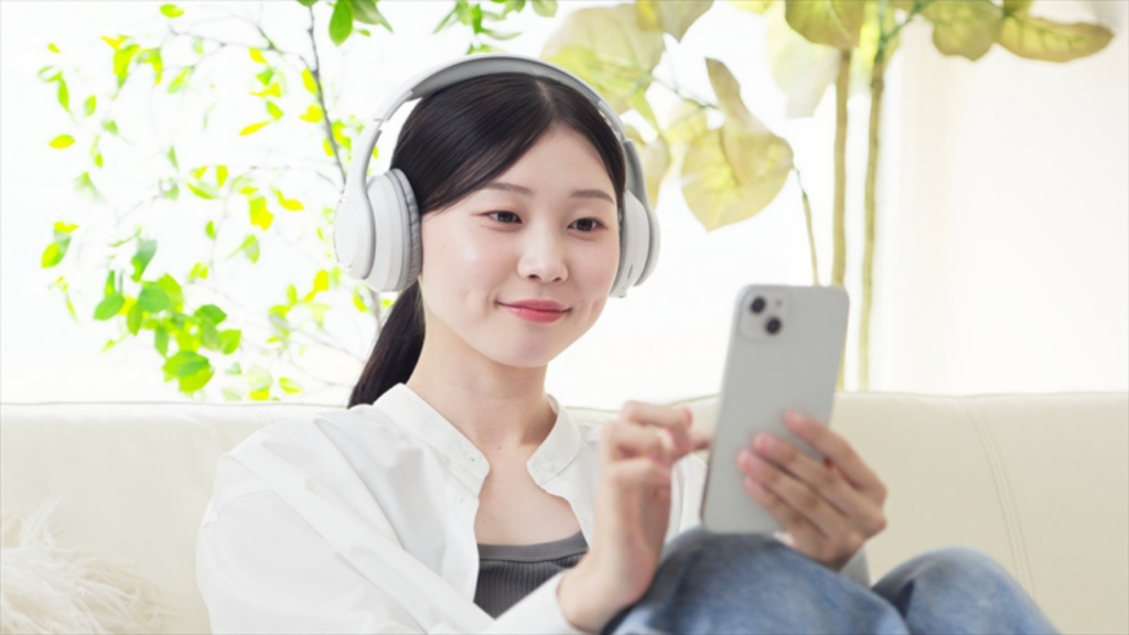 ヘッドフォンをしながらソファでスマホを見る女性