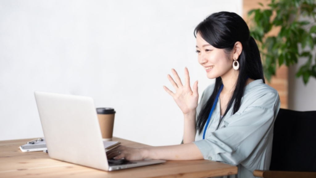 パソコンに向かって右手を上げる女性